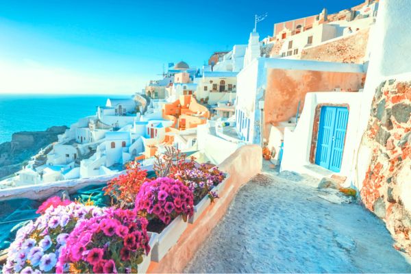 خانههای سفید و آبی با گلهای رنگارنگ در جزیره سانتورینی یونان، با چشمانداز دریای اژه. - یونان چند جزیره دارد