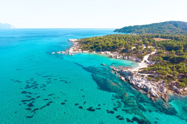 نمای هوایی از سواحل بکر و آبهای شفاف دریای اژه در یونان با جنگلهای سرسبز و صخرههای ساحلی. - یونان چند جزیره دارد