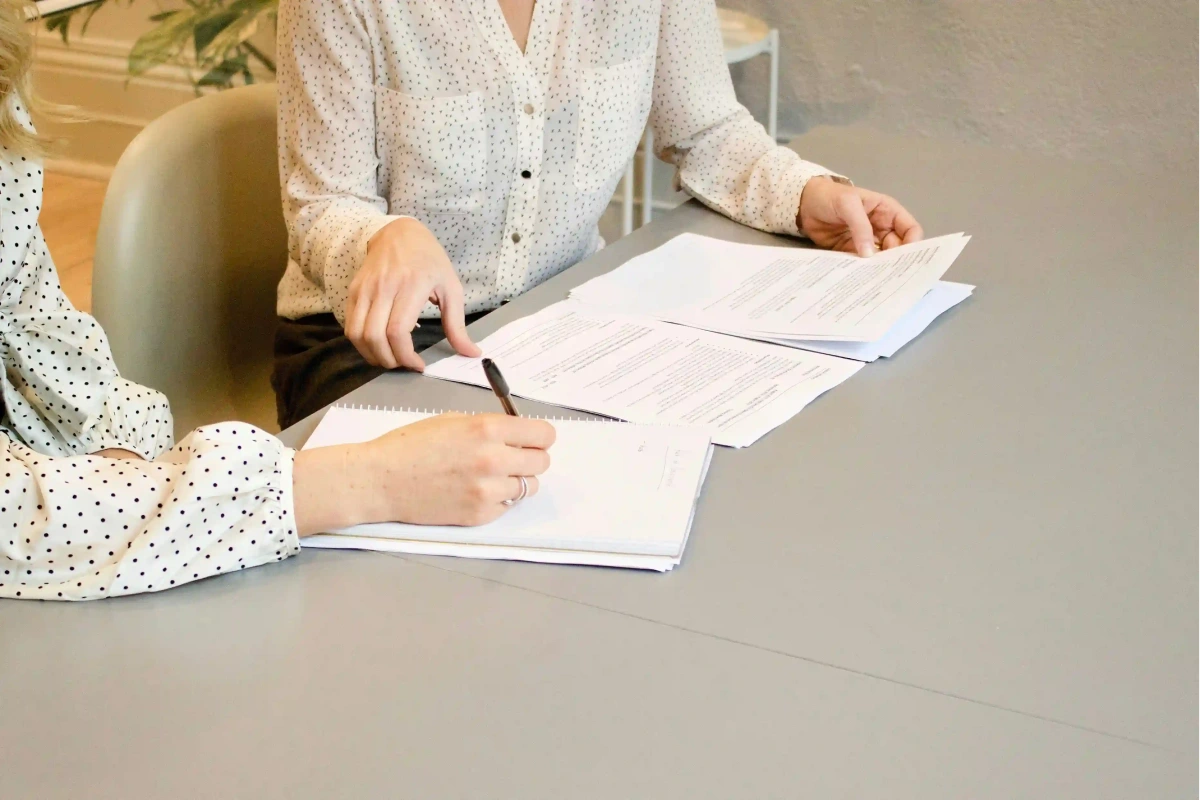 نمایی نزدیک از دو نفر در حال بررسی مدارک و نوشتن در یک جلسه کاری. این تصویر فرآیند ارائه مشاوره ثبت شرکت در امارات و بررسی اسناد لازم را به تصویر می‌کشد.